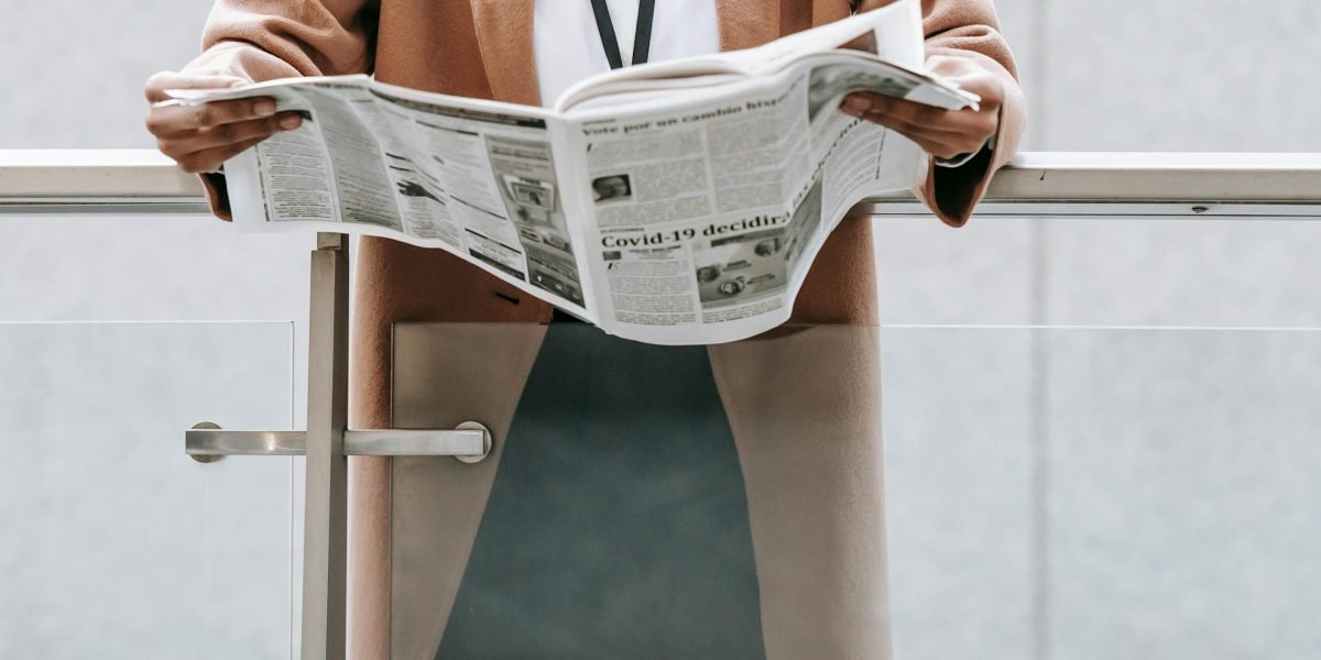 A business professional looks thoughtfully at a newspaper, reflecting concern about content or reputation.